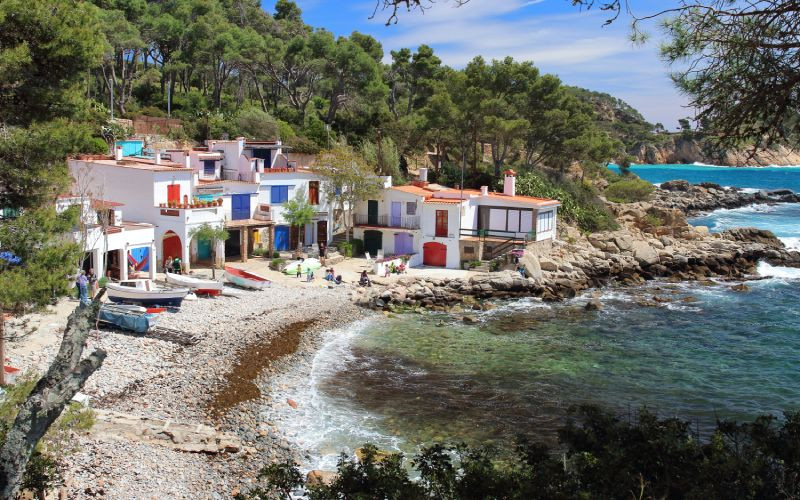 Crique rocheuse, petites maisons aux portes colorées sur fond de pins